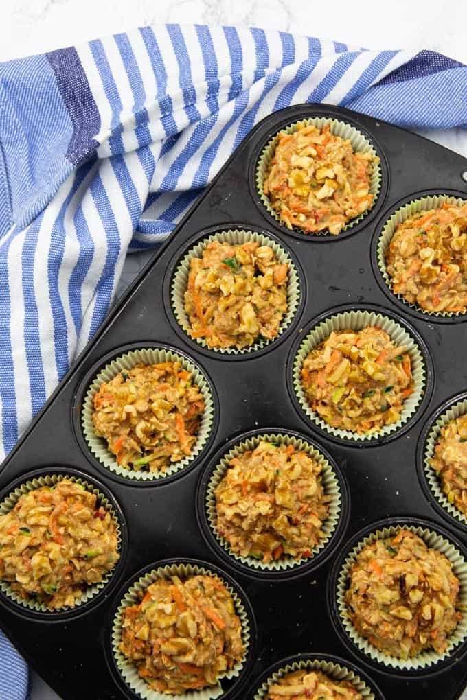 unbaked zucchini carrot muffin batter in paper liners in a muffin tray sprinkled with chopped walnuts 