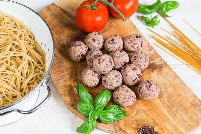 uncooked vegan meatballs on a wooden board with cooked spaghetti in a colander 