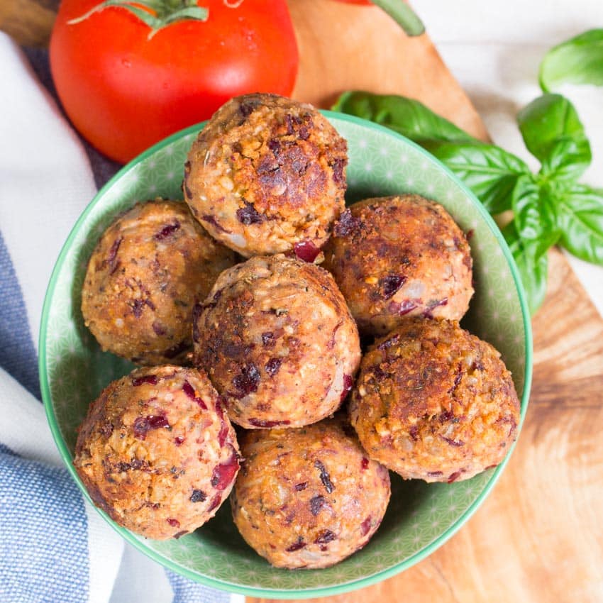 a stack of vegan meatballs in a green bowl with a tomato and basil on the side