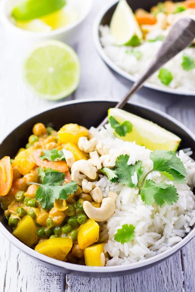 vegan chickpea curry with jasmine rice in a black bowl on a white wooden surface with limes and another bowl in the background