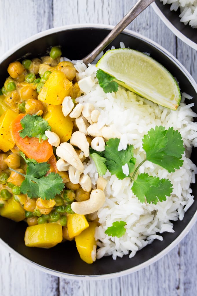 vegan curry in a black bowl with Jasmine rice, cilantro, and a lime wedge on a white wooden surface 