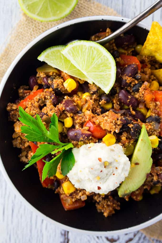 vegan chili in a black bowl with two lime wedges, fresh cilantro, avocado, and sour cream on top 