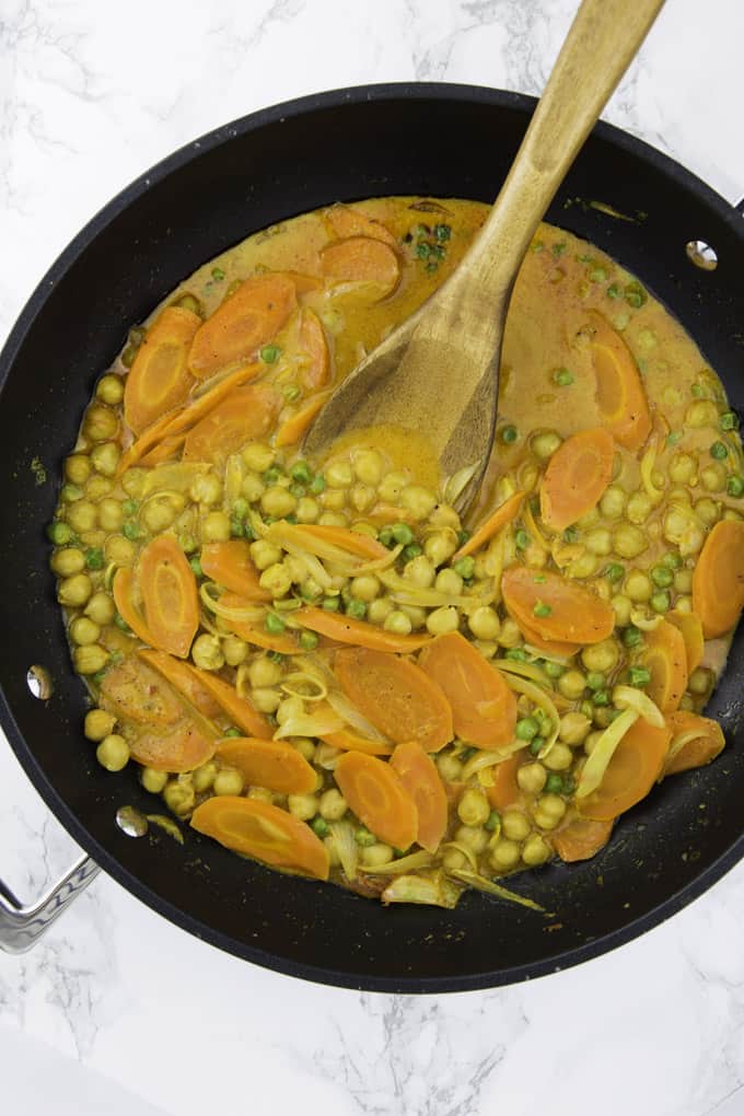 vegan chickpea curry in a black pan with a wooden spoon on a marble counter top