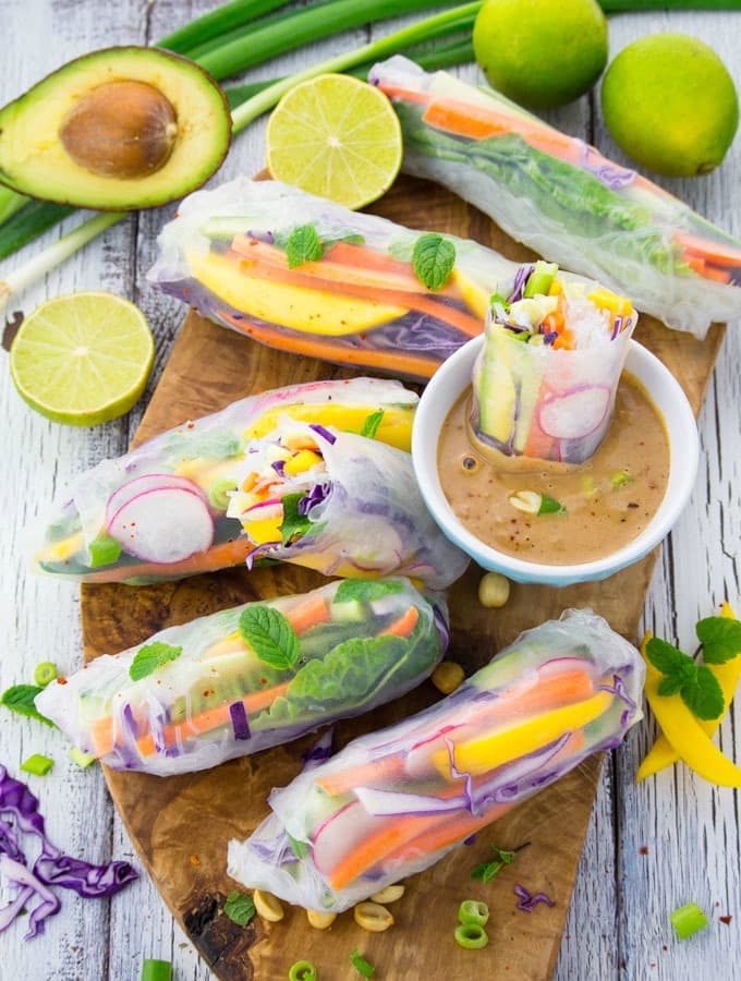Rice Paper Rolls on a wooden board with a small bowl of peanut sauce, three limes, and half an avocado on the side 