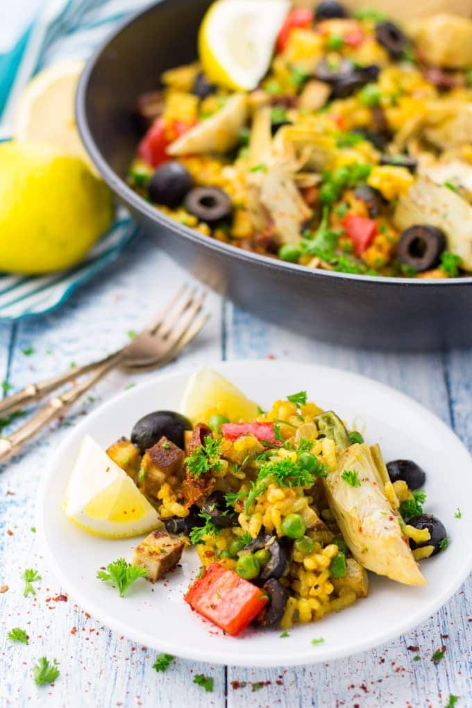 Vegan Paella with lemon wedges on a white plate with a black pan with more paella and two forks in the background