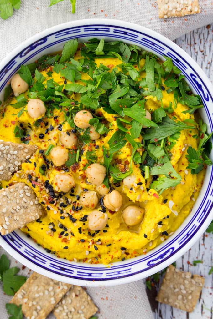 pumpkin hummus with fresh parsley on top in a blue and white bowl with sesame crackers on the side