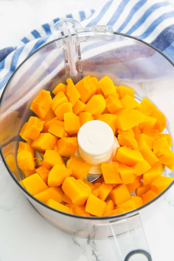 cooked pumpkin cubes in a food processor on a marble counter top
