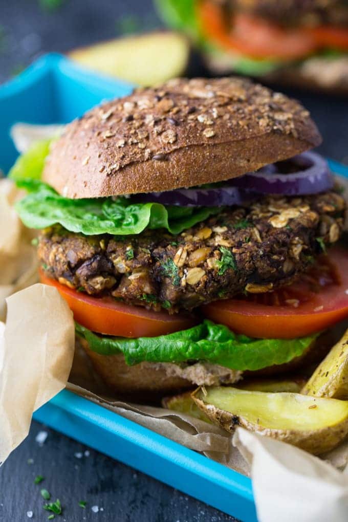 close-up de um hambúrguer de cogumelos vegan numa bandeja azul com batatas fritas de lado