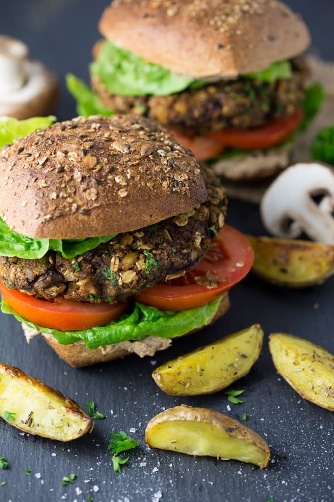 Zwei Champignon-Burger auf einer schwarzen Arbeitsplatte mit Pommes und Champignons an der Seite