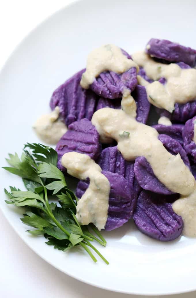 purple sweet potato gnocchi with tahini sauce on a white plate with fresh parsley on the side