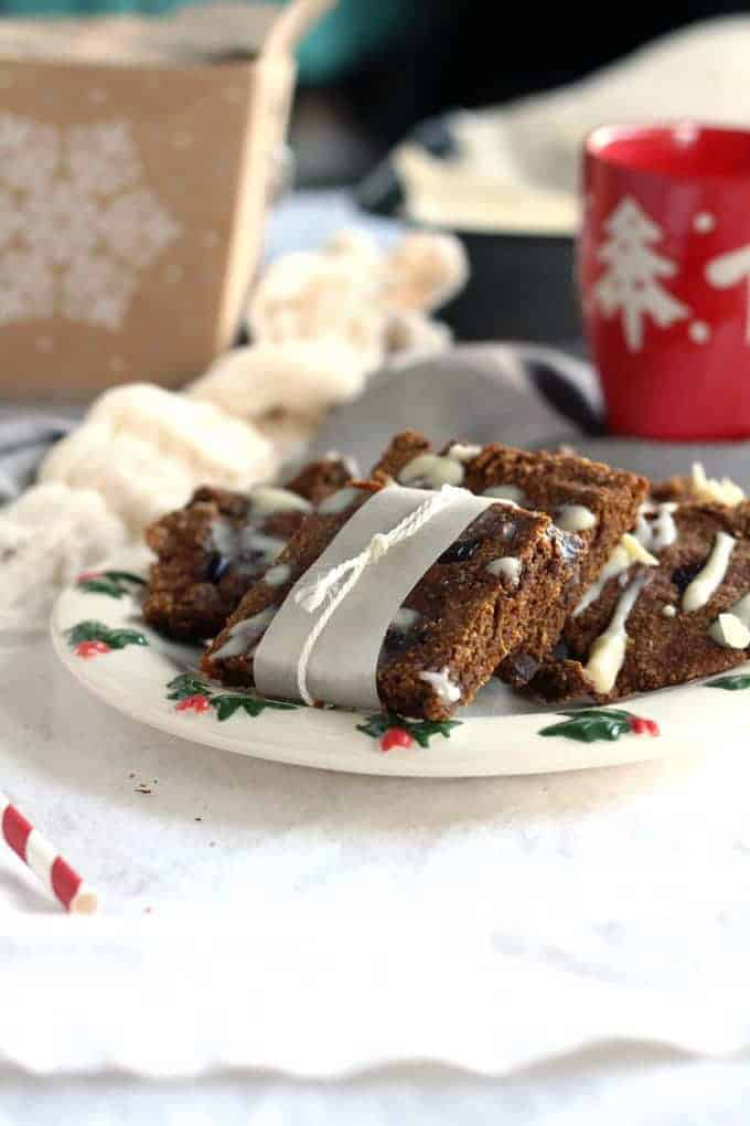cranberry gingerbread bars on a white plate with a red Christmas mug in the background and a sugar cane on the side 
