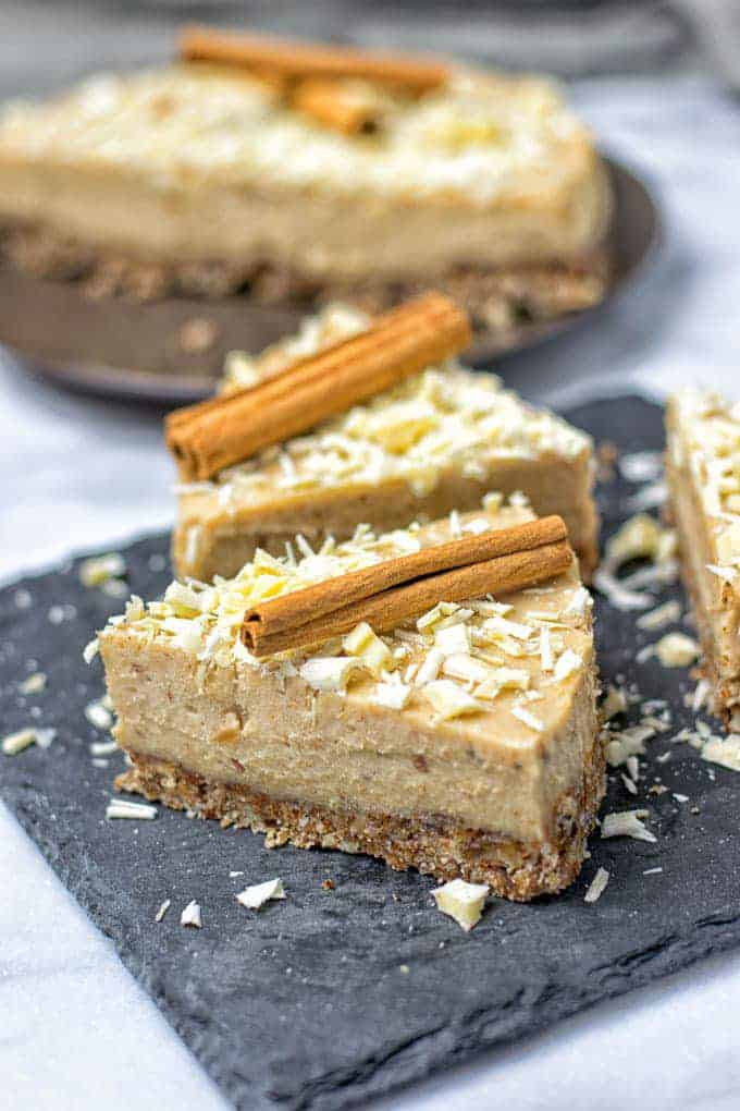 two slices of vegan cinnamon cheesecake on a black serving plate with more cake in the background