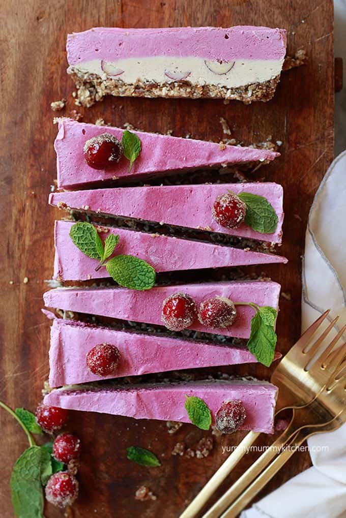 seven slices of cranberry no bake cheesecake on a wooden board with three forks and mint leaves on the side 