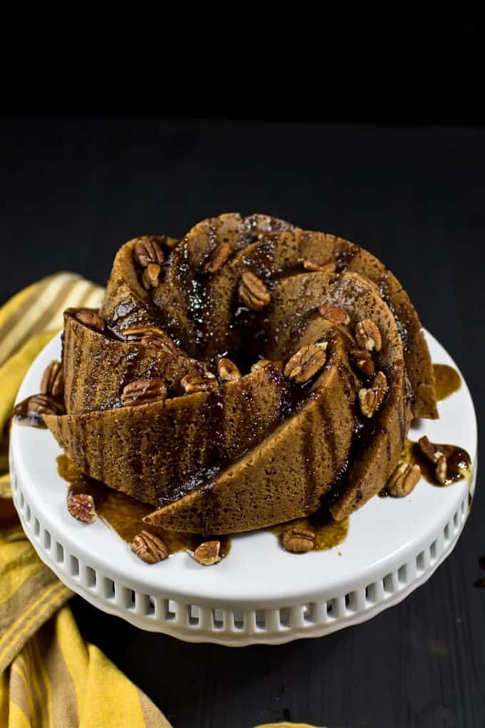 a vegan cinnamon bundt cake on a white serving plate with a yellow dish cloth on the side on a black surface 