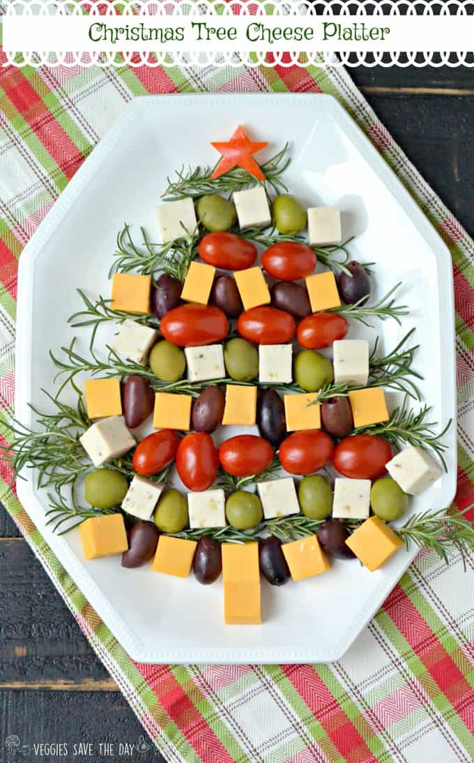 a vegan cheese platter with cherry tomatoes and olives formed to a Christmas tree on a white plate 