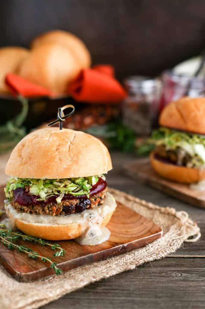 a vegan holiday burger with Brussels sprouts slaw and vegan mayonnaise on a wooden board with another burger in the background
