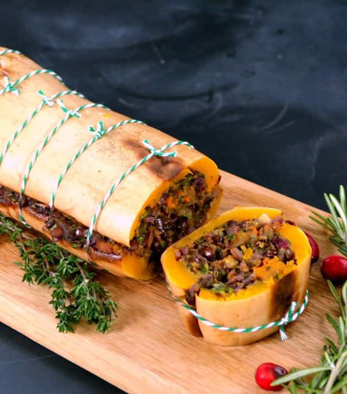 a butternut roast with one slice on a wooden board with fresh rosemary and cranberries on the side