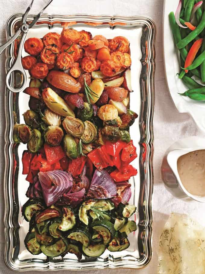 roasted carrots, Brussels sprouts, bell pepper, zucchini, and red onion on a serving plate with gravy and a plate of green beans on the side