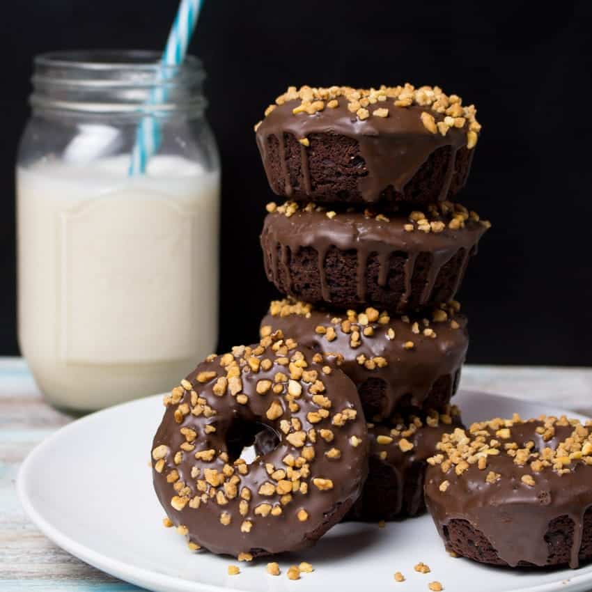 six vegan chocolate donuts on a white plate with a glass of milk in the background