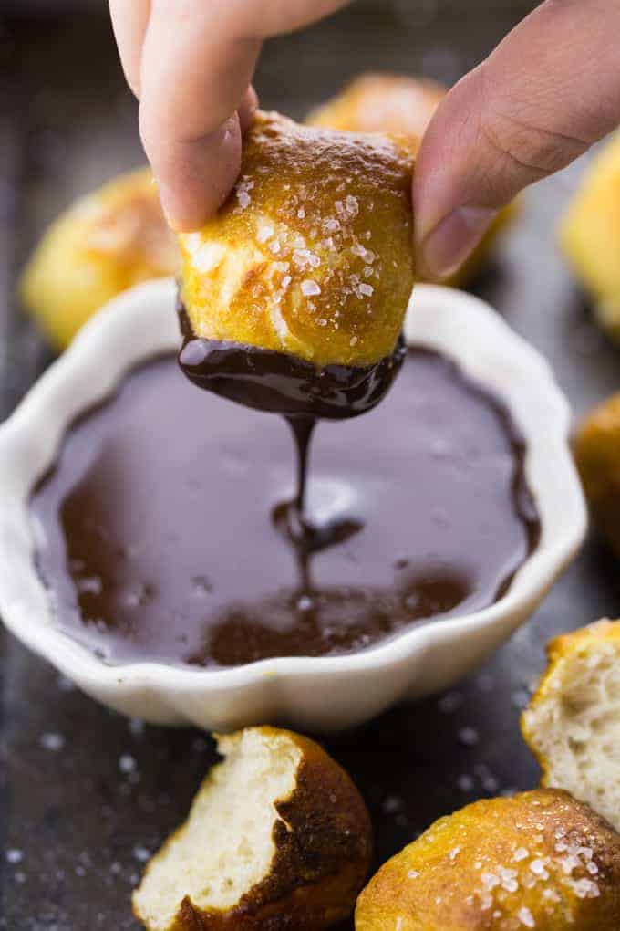 a hand dipping a vegan pretzel bite into a small bowl of chocolate sauce with more pretzel bites on the side 