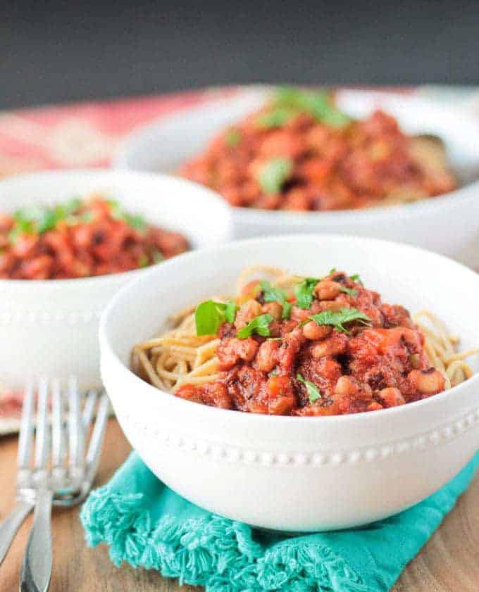 three white bowls of smoky cajun black eyed peas pasta on a wooden board with two forks on the side 