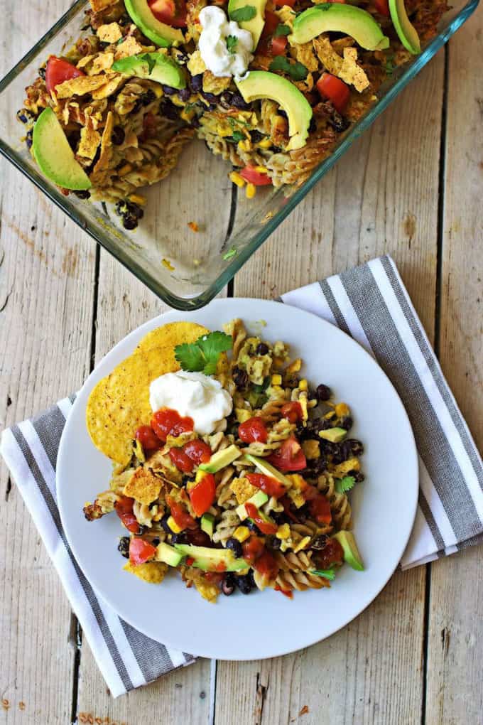 a plate with Mexican pasta bake on a wooden board with a casserole dish with the rest of the casserole in the background 