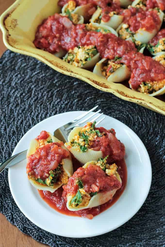pumpkin and kale stuffed shells on a white plate with a fork and a casserole dish with more shells in the background