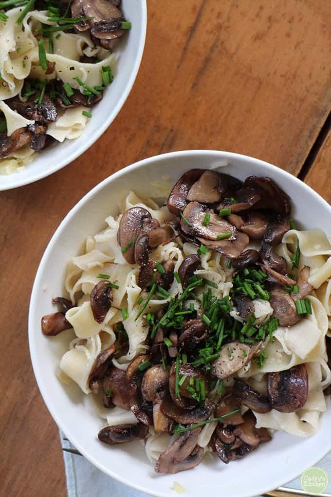 two bowls of vegan buttered noodles with red wine mushrooms on a wooden counter top 