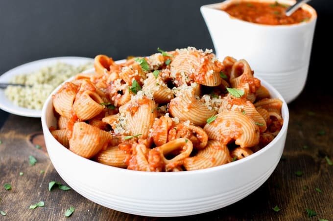 a bowl of pasta with vegan meat sauce with a plate of vegan parmesan and vegan meat sauce in the background