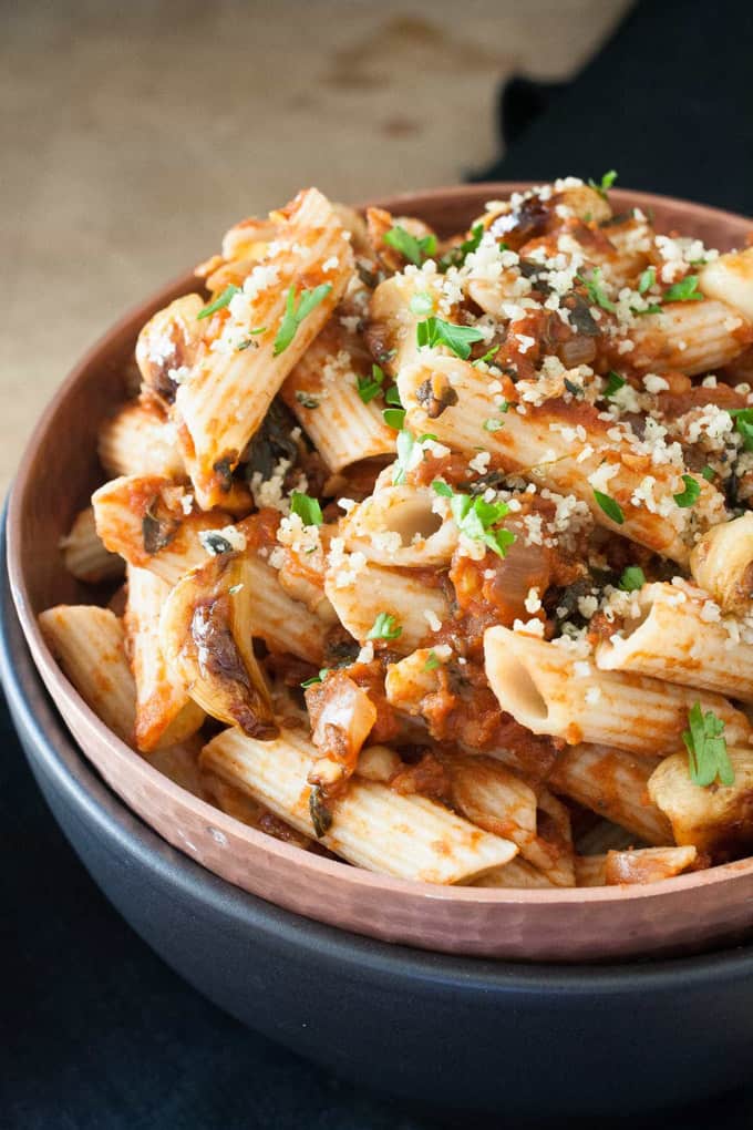 pasta with vegan spicy tomato sauce and chickpeas in a brown bowl with a black bowl underneath 