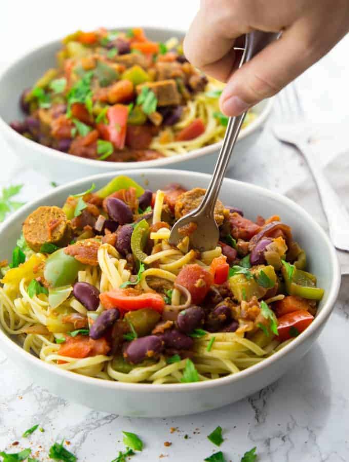 two bowls of vegan Cajun pasta and a hand rolling up pasta with a fork