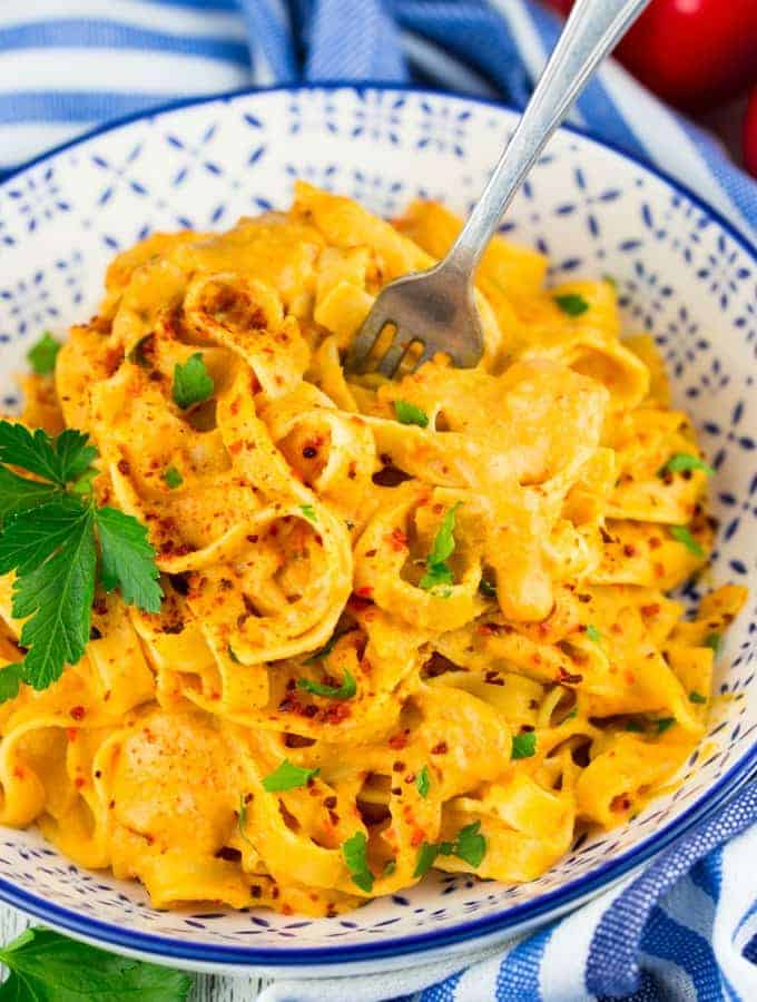 fettuccine with red pepper sauce in a blue and white bowl with a fork and a blue dish cloth in the background 