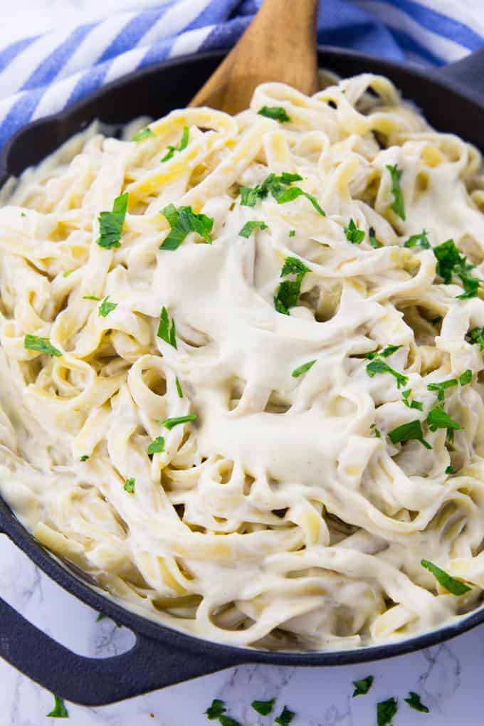 a pan of fettuccine with vegan Alfredo sauce on a marble counter top with a blue and white dish cloth in the background