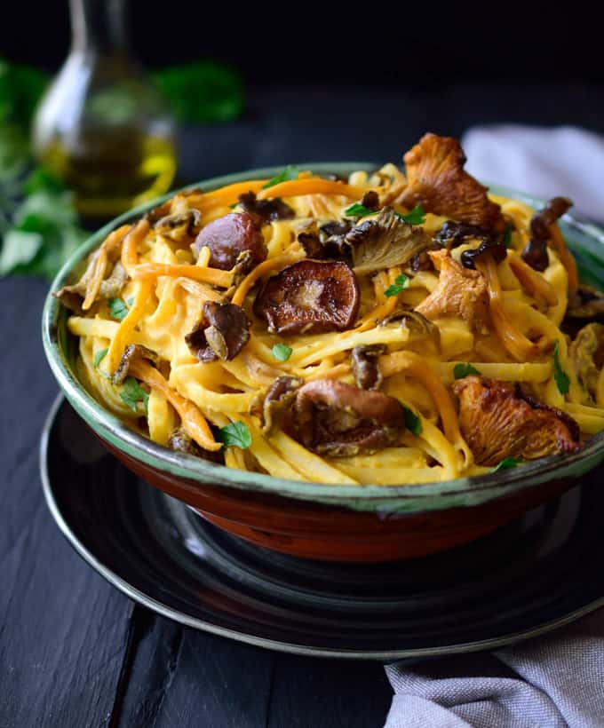 a bowl of pasta with pumpkin sauce and mushrooms on a dark wooden surface with a white dish cloth in the background