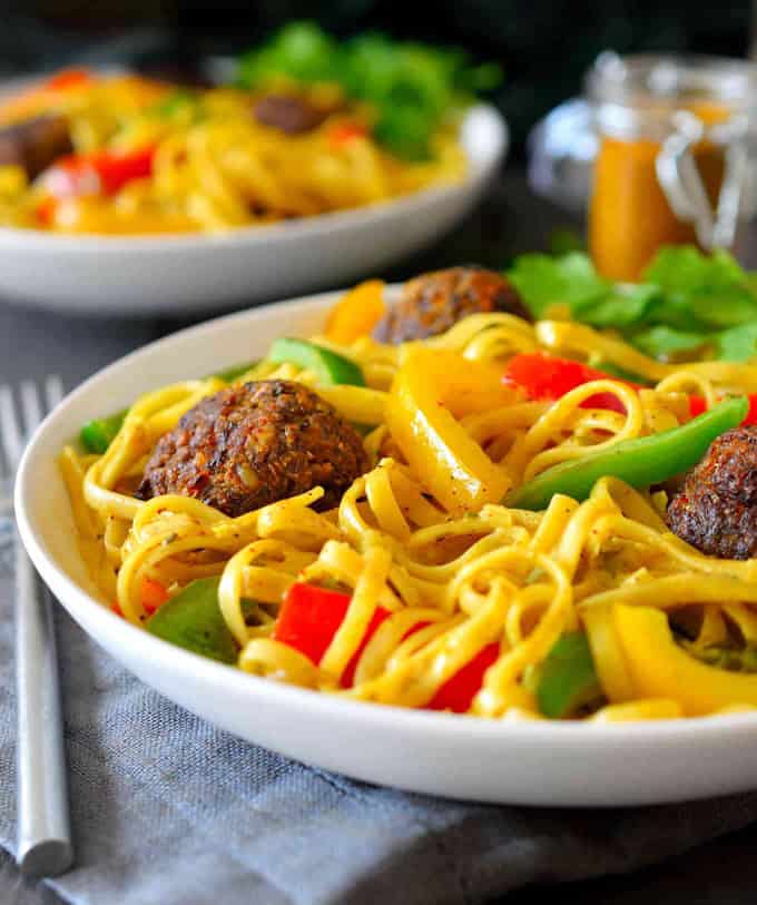 vegan rasta pasta in two white bowls with walnut balls, bell peppers, and coconut curry sauce with a grey dish cloth and a fork on the side 