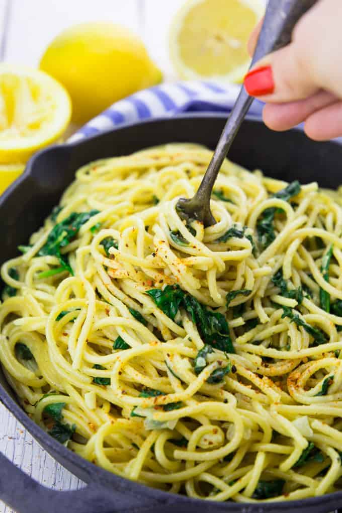 vegan lemon pasta in a cast-iron pan with lemons in the background and a hand rolling up spaghetti with a fork