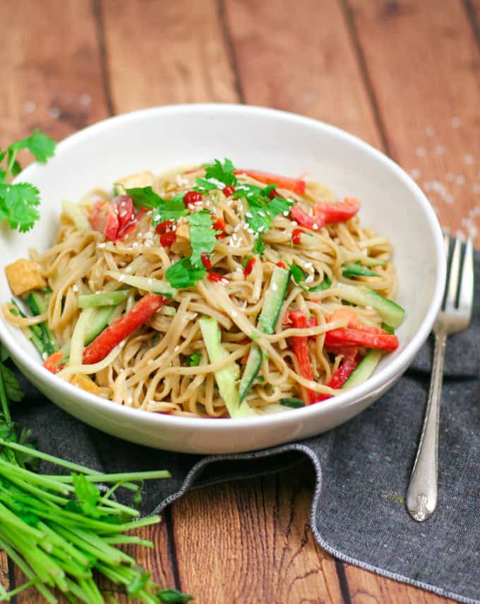 chilled peanut noodle with crispy tofu and bell peppers on a wooden board with a fork on the side 