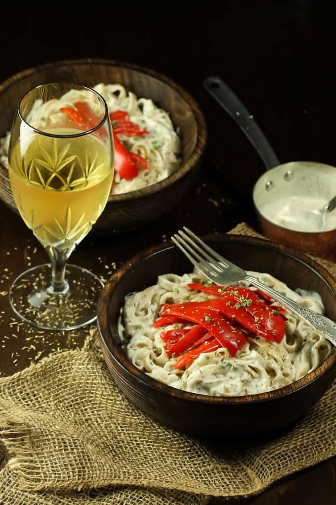 two bowls of creamy vegan white wine pasta with roasted red peppers on top and a glas of white wine on the side