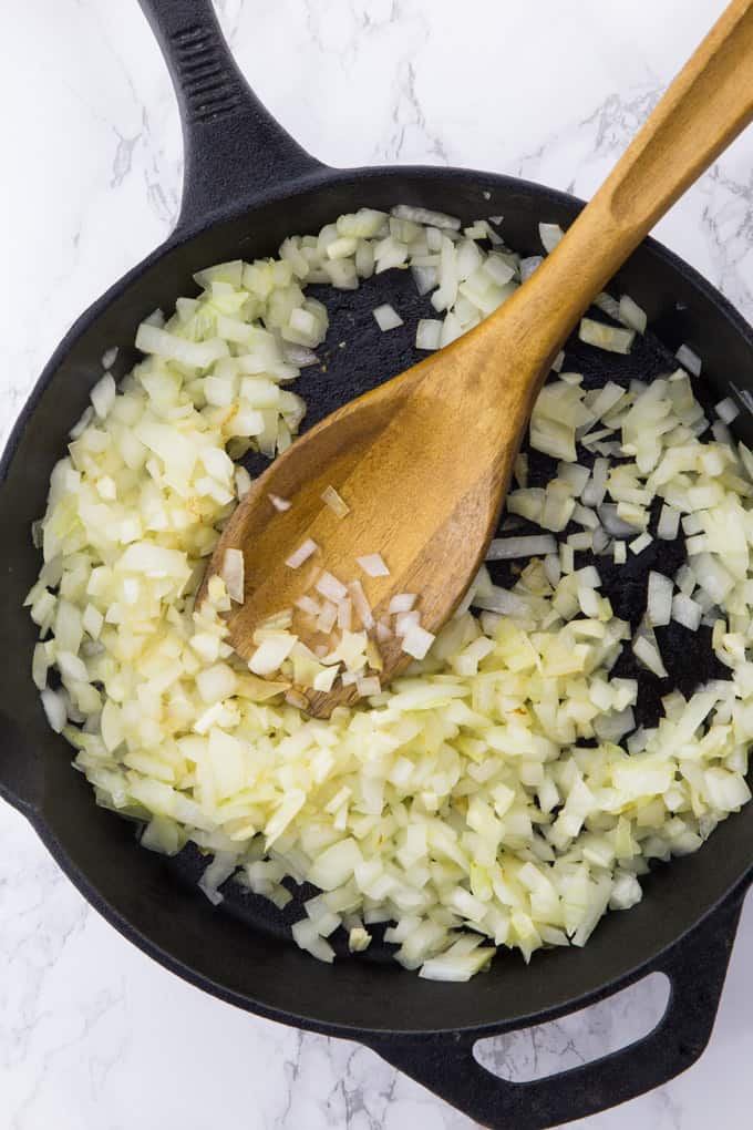 chopped onions are being sauted in a cast iron pan with a wooden spoon