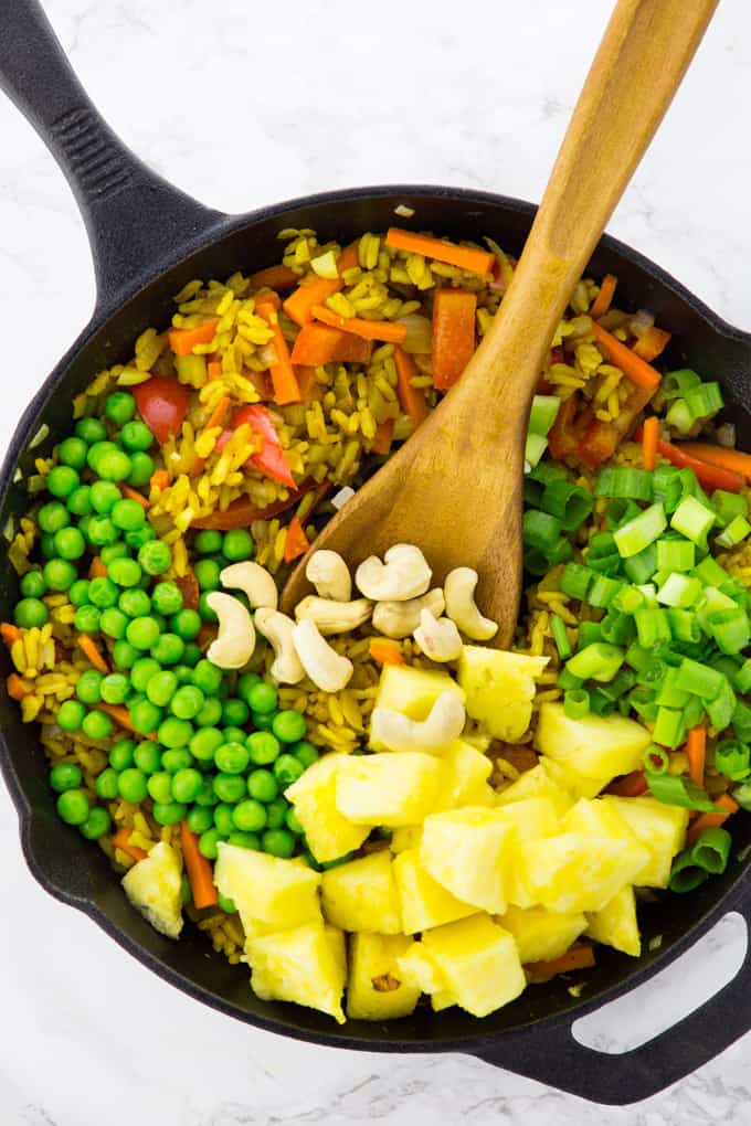 Thai fried rice in a cast iron skillet with peas, pineapple chunks, and cashews on top
