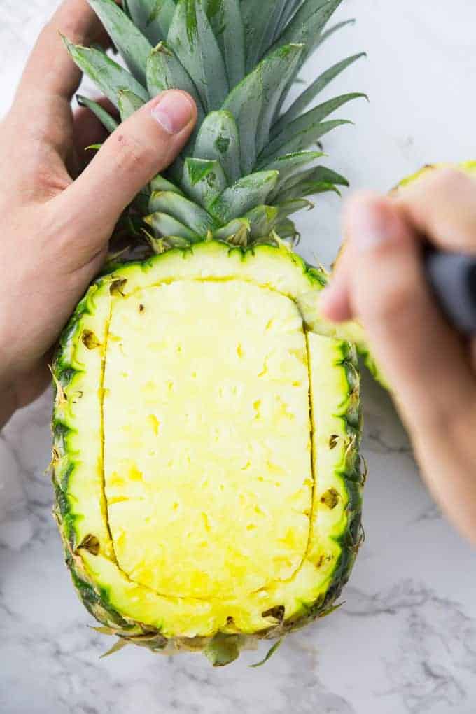 A pineapple being cut into a bowl