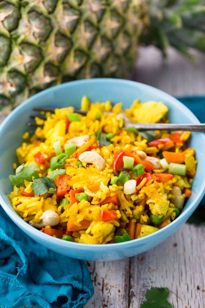 pineapple fried rice in a blue bowl with a fork with a pineapple in the background