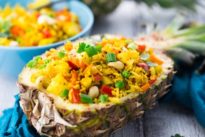 Thai Pineapple Fried Rice in a Pineapple Shells with a Blue Bowl of Rice in the Background