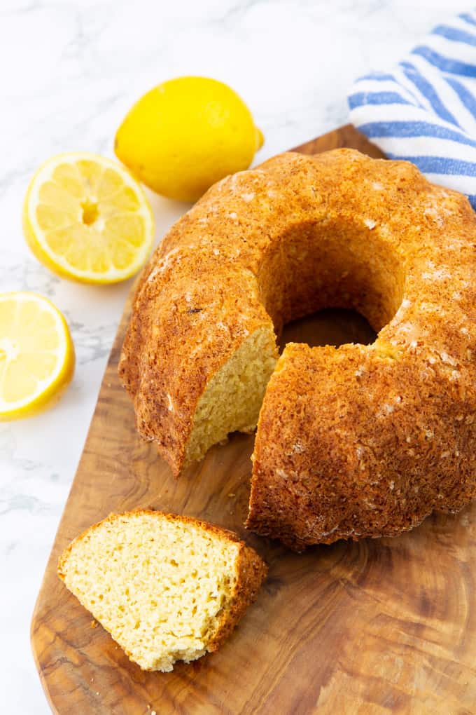 a vegan lemon cake on a wooden board on a marble countertop with lemons in the background