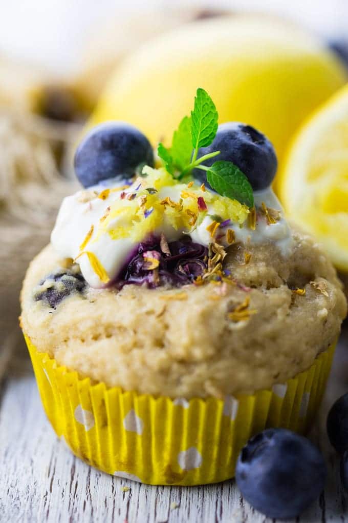 a close-up of a vegan blueberry muffins on a white wooden board with lemons in the background 