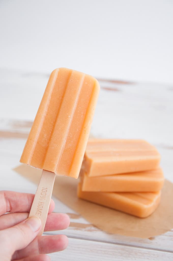 a hand holding a cantaloupe lucuma popsicle with a stack of three popsicles in the background 