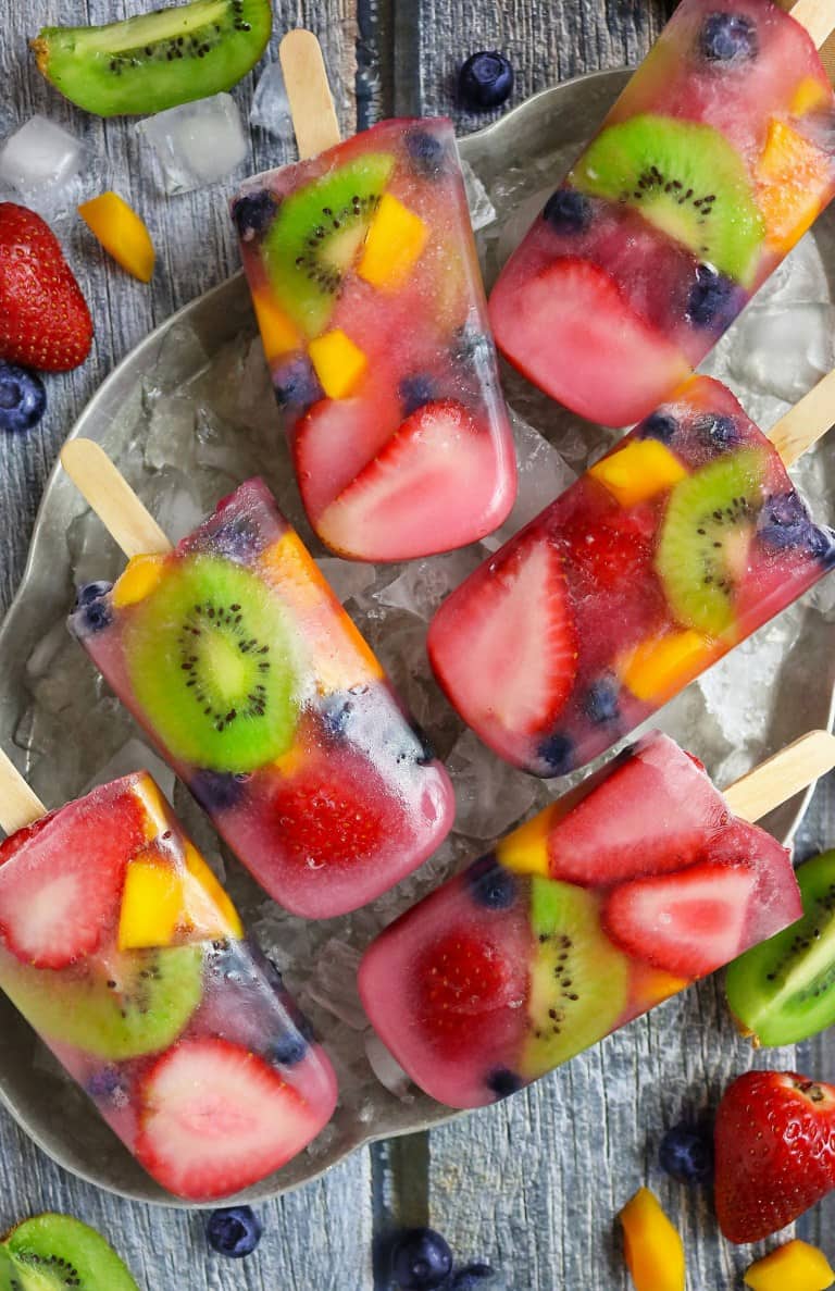 six fruit popsicles in a bowl with ice cubes and sliced fruits on the side 