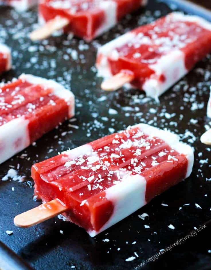 four strawberry rhubarb popsicles with coconut flakes on top on a black cutting board 