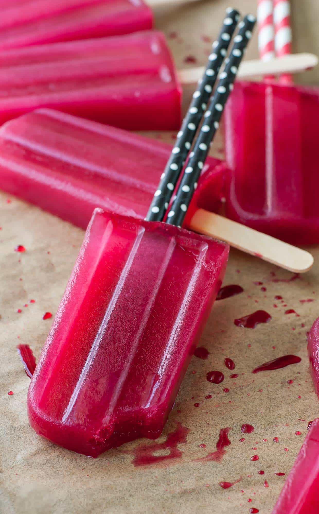 five green tea hibiscus popsicles on parchment paper with black and white straws 