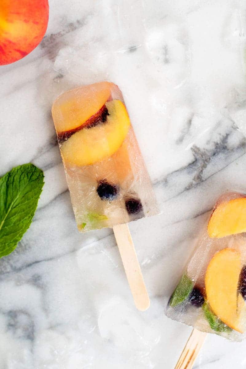 two peach sangria popsicles on a marble countertop with a peach and a mint leaf on the side 